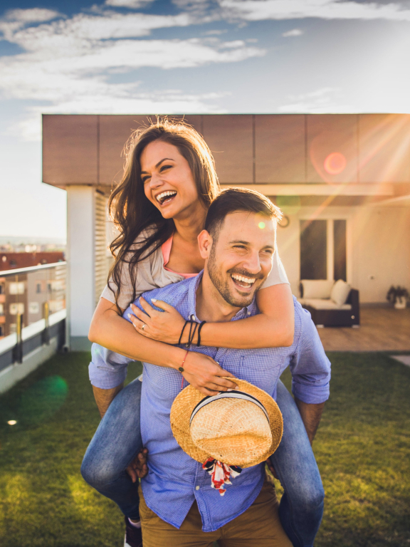 Glückliches Paar feiert den Umzug in ihr neues Zuhause auf der Dachterrasse mit Blick über die Stadt bei Sonnenuntergang.