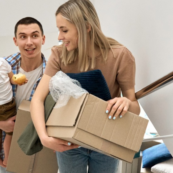 Eine glückliche Familie trägt beim Auslandsumzug voller Vorfreude Umzugskartons in ihr neues Zuhause mit Unterstützung von DACHSER & KOLB.