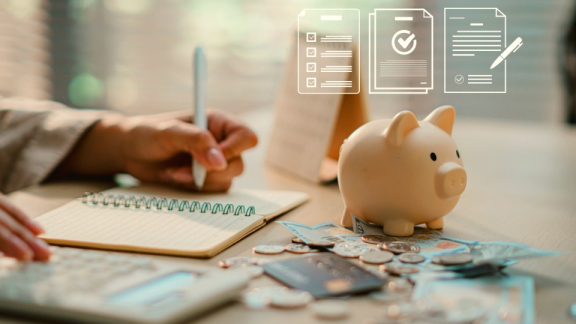Ein Sparschwein mit Bargeld, einer Kreditkarte und einem Taschenrechner zur Planung von Finanzen, Budget und Steuern beim Auslandsumzug mit DACHSER & KOLB.
