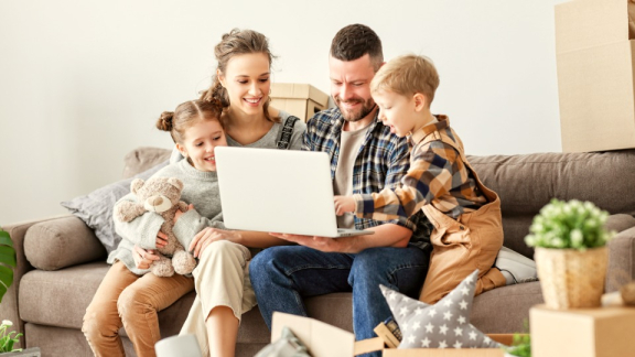 Eine glückliche Familie berechnet gemeinsam am Laptop die Kosten für den Umzug in die Schweiz mit dem digitalen Umzugskostenrechner von DACHSER & KOLB.