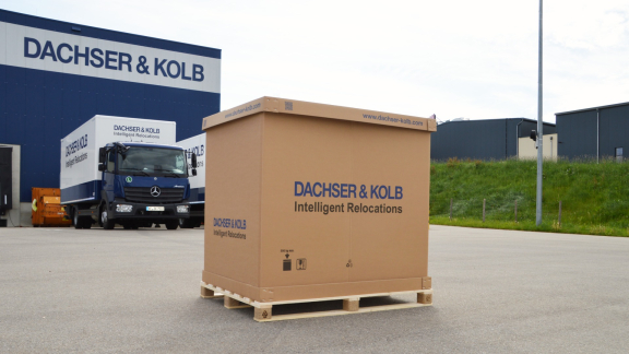 Eine große DACHSER & KOLB Palettenbox auf einer Holzpalette vor Firmen-Lkw, genutzt für den sicheren Kleintransport von Möbeln und Kartons.