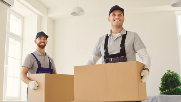 Zwei professionelle Umzugshelfer von DACHSER & KOLB beim Kleintransport mit Umzugskartons im Zwei-Mann-Handling.