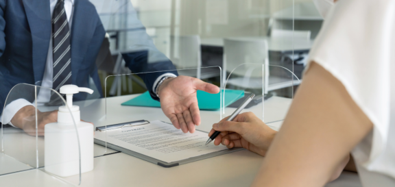 Person unterschreibt Formular zum Unmelden nach dem Umzug in einem Bürgerbüro hinter Plexiglasscheibe.