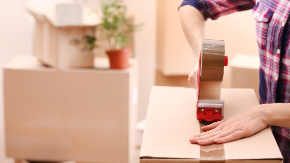 Nahaufnahme einer Person, die einen Umzugskarton mit Klebeband verschließt. Symbol für Relocation Service für Expats.