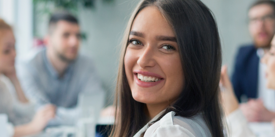Eine lächelnde junge Frau im Vordergrund einer Gruppe während einer Ausbildungsveranstaltung.