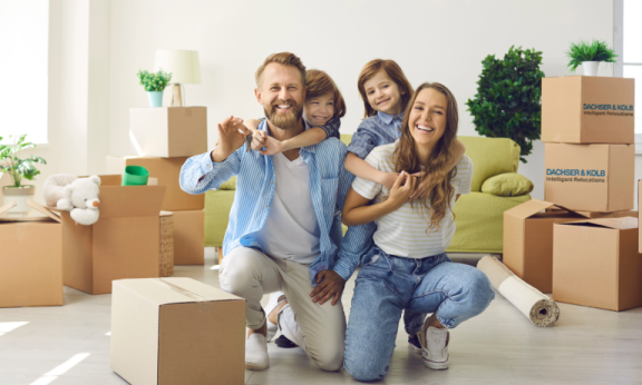 Lächelnde Familie posiert zwischen Umzugskartons beim VIP-Umzug für prominente Persönlichkeiten in neues Zuhause