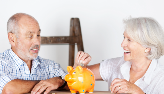 Seniorenpaar spart gemeinsam für Seniorenumzug in gehobene Wohnresidenz – lachend mit Sparschwein