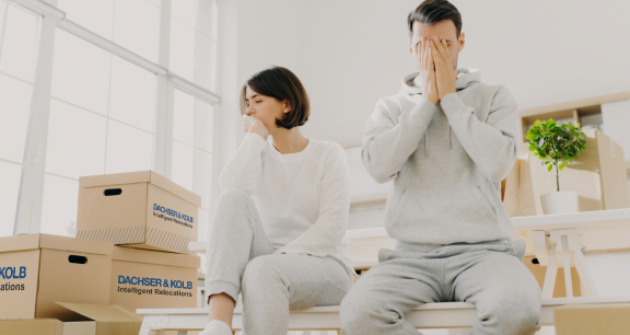 Erschöpftes Paar sitzt zwischen Umzugskartons. Stressmanagement während des Umzugs: Müdigkeit und Frustration.