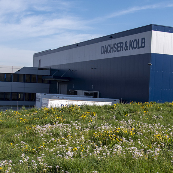 Modernes Gebäude des Umzugsunternehmens DACHSER & KOLB mit Lagerhalle und Bürotrakt, umgeben von grüner Wiese.