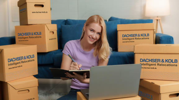 Frau lächelt mit Umzugsplanung zwischen Umzugskartons.