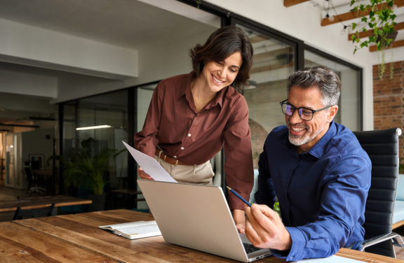 Zwei Kollegen besprechen lächelnd am Laptop Details zum Sonderurlaub für Umzug im modernen Büro.