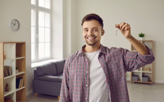 Junger Mann hält Schlüssel in neuer Wohnung – Tipps für den Einzug in die erste eigene Wohnung