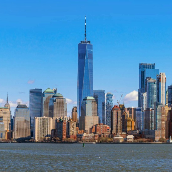 Auswandern nach USA – Freiheitsstatue vor Skyline von New York City bei blauem Himmel