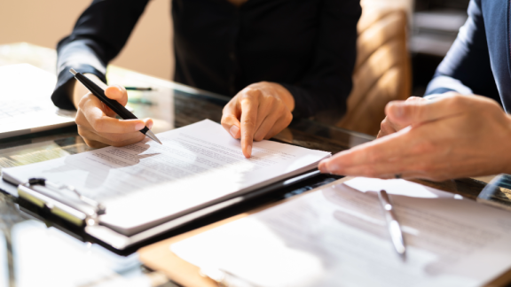 Zwei Personen am Schreibtisch unterschreiben einen Vertrag.