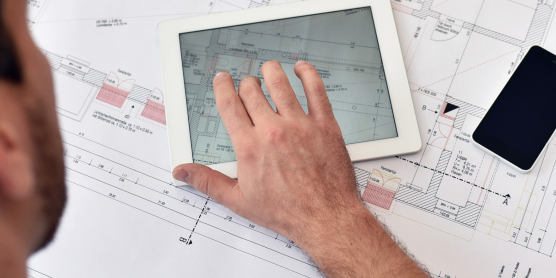 Projektleiter analysiert den Grundriss auf einem Tablet fuer die lueckenlose Standortverlagerung.