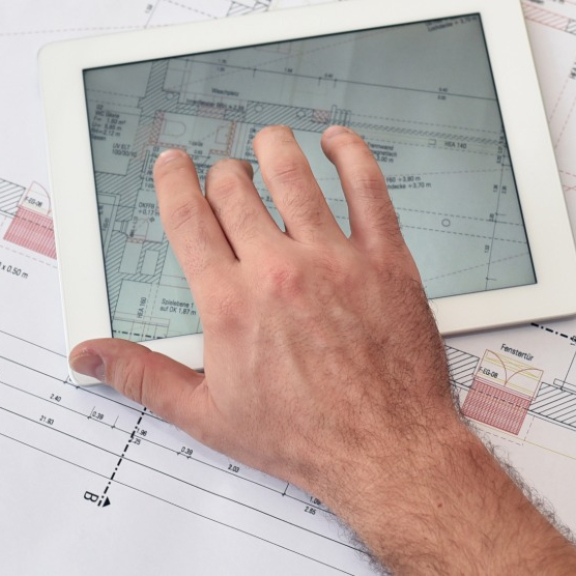 Projektleiter analysiert den Grundriss auf einem Tablet fuer die lueckenlose Standortverlagerung.