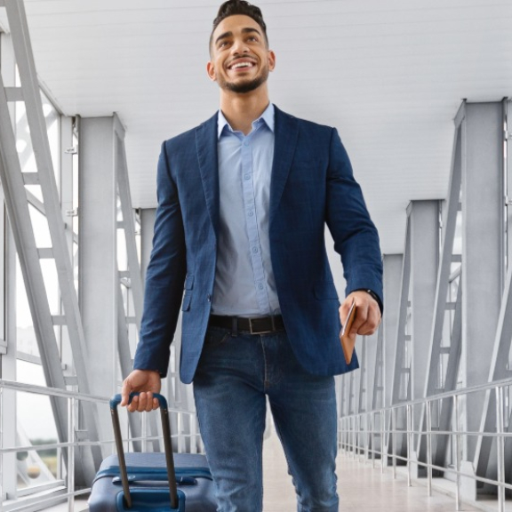 Ein lächelnder Expat im Business-Outfit zieht seinen Rollkoffer durch ein modernes Flughafenterminal zu einem internationalen Auslandseinsatz.