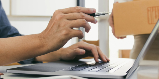 Eine Koordination am Laptop neben einem Umzugskarton und Paketband für die strategische Beschaffung von Moving- und Relocation-Leistungen im B2B-Procurement.