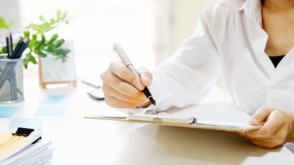 Compliance im B2B-Prozess bei DACHSER und KOLB – Eine Person unterschreibt Dokumente auf einem Klemmbrett mit einem Füllfederhalter am Schreibtisch.