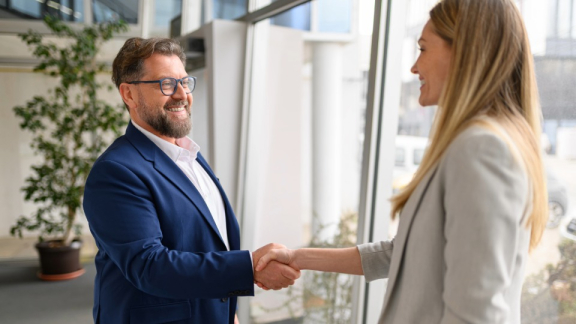 Erfolgreicher B2B-Projektabschluss bei DACHSER und KOLB – Ein lächelnder Projektmanager im blauen Anzug gibt einer Kundin im modernen Büro die Hand.