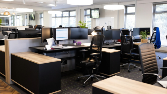 Flächenoptimierung beim Büroumzug – Ein modernes, helles Großraumbüro mit ergonomischen Schreibtischen und Computerbildschirmen.