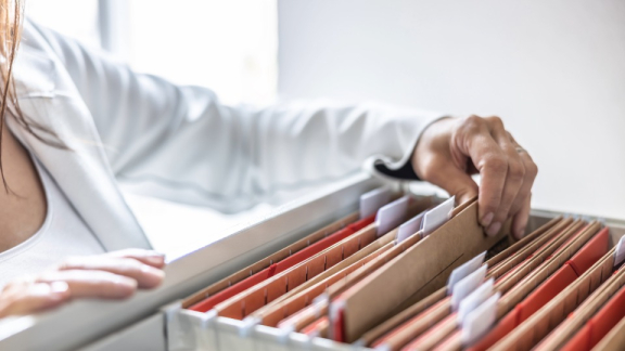Datensicherheit beim Behördenumzug – Eine Mitarbeiterin sortiert vertrauliche Dokumente in Hängeregister-Ordnern in einer Archivschublade.