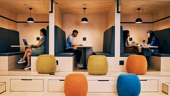 Mitarbeitende arbeiten mit Laptops in modernen Sitzboxen eines flexiblen Coworking-Büros im New Work Design.