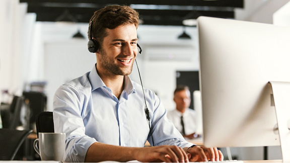 Ein freundlicher DACHSER & KOLB Projektmanager mit Headset berät HR-Kunden am PC zum aktuellen Status einer Mitarbeiterentsendung.