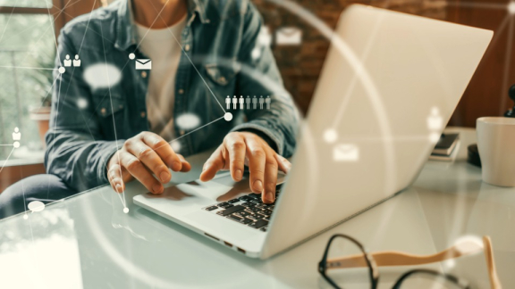 Eine Person arbeitet am Laptop mit eingeblendeten Icons für HR-Netzwerke und Mitarbeiterkapazitäten – Skalierbarkeit im Procurement für weltweite Mitarbeiterumzüge.