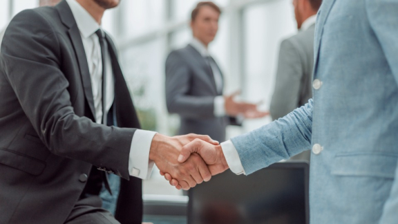 Zwei Geschäftspartner besiegeln eine strategische Partnerschaft per Handschlag – Single Sourcing und Kostenoptimierung für globale Mobilitätsanforderungen.