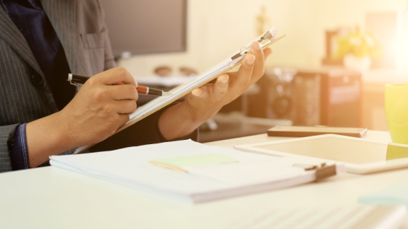 Eine Person im Business-Outfit prüft und dokumentiert Leistungsnachweise auf einem Klemmbrett im Büro – Für standardisierte Abrechnung und Revisionssicherheit im Einkauf.