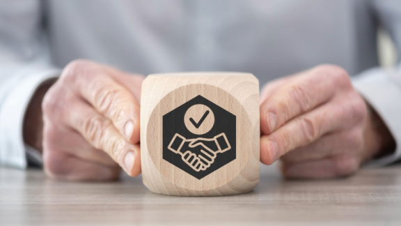 Ein Holzwürfel mit einem Händeschütteln-Symbol als Zeichen für ausgezeichnete Zuverlässigkeit bei B2B-Projekten mit DACHSER & KOLB.