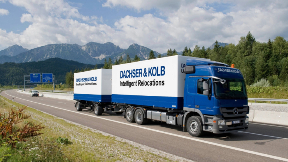Ein blauer LKW-Zug von DACHSER & KOLB fährt auf einer Autobahn vor Bergen und symbolisiert das starke Logistiknetzwerk für professionelle Firmenumzüge.
